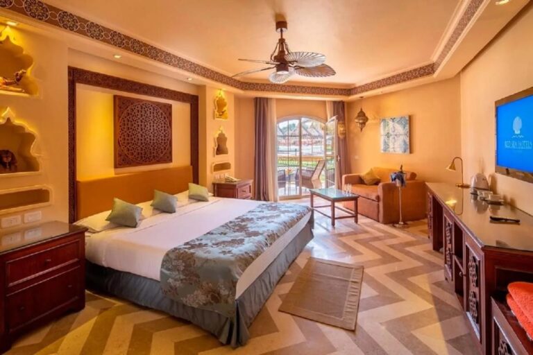 Una habitación con cama grande, hornacinas iluminadas, ventilador de techo y una puerta acristalada que da al balcón