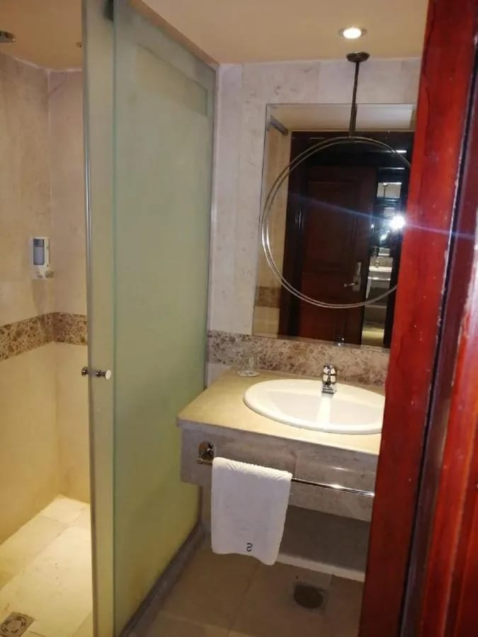 Una ducha de cristal y un lavabo bajo un espejo redondo
