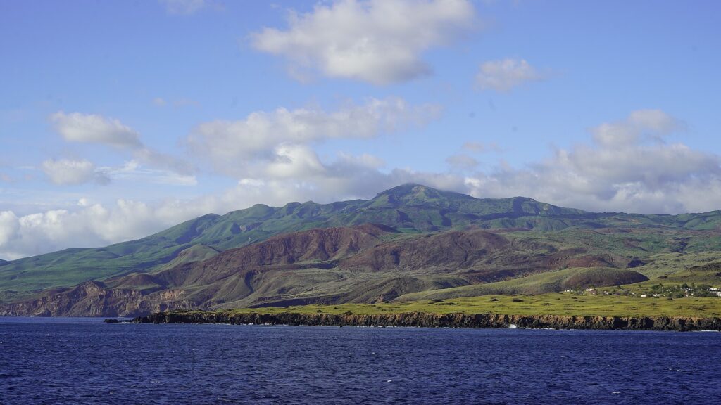 La costa de la isla Socorro vista desde el mar: acantilados de lava negra, colinas verdes y rojizas y la cima del volcán entre las nubes