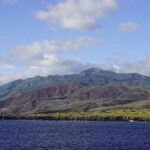 La costa de la isla Socorro vista desde el mar: acantilados de lava negra, colinas verdes y rojizas y la cima del volcán entre las nubes