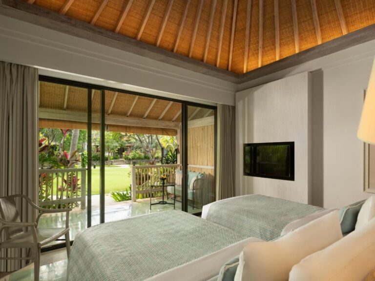 Una habitación con dos camas y techo de madera, con un ventanal que da al jardín