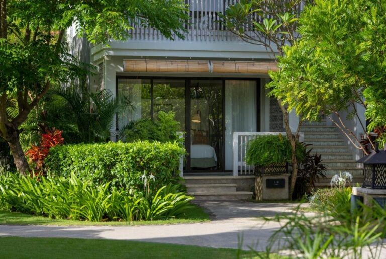 La entrada de un edificio de habitaciones, rodeada de plantas tropicales