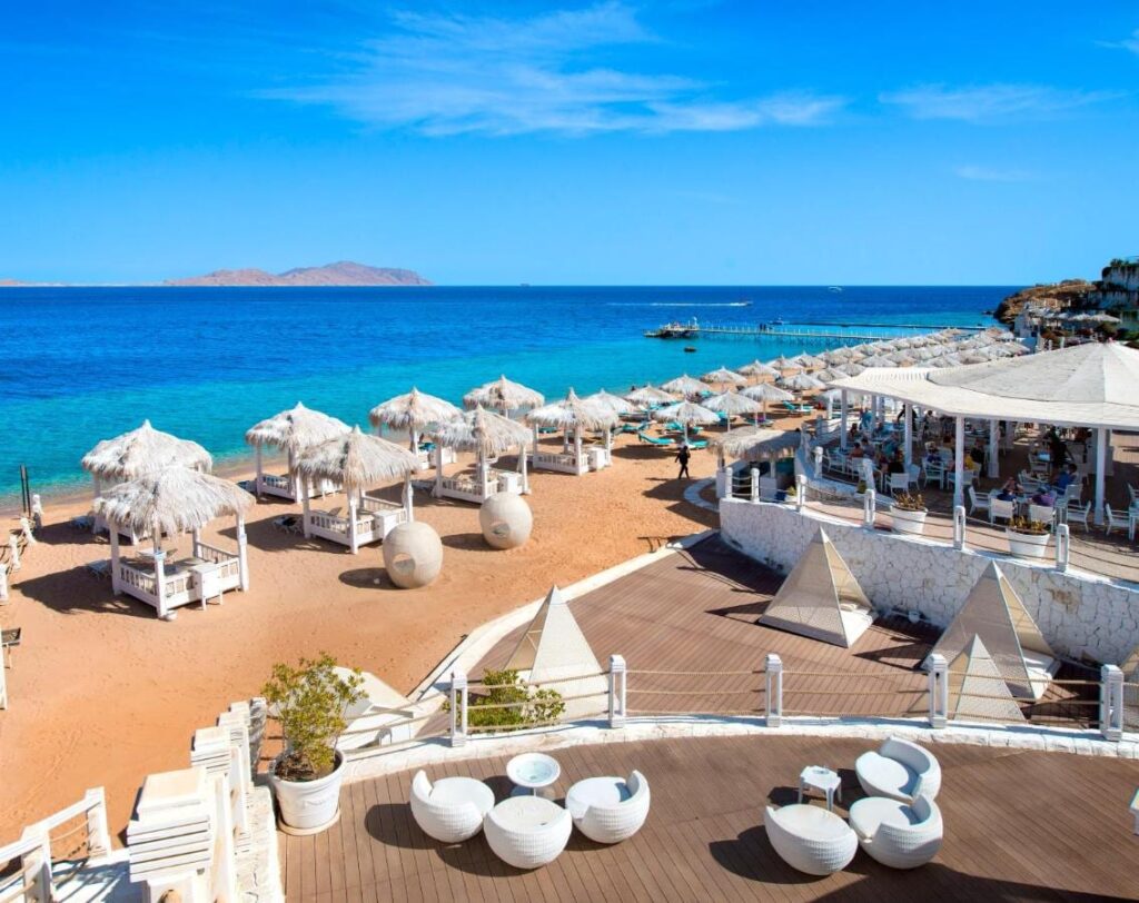 La playa del Sunrise Arabian Beach Resort, con sus sombrillas de paja y su pontón, frente a la isla de Tiran