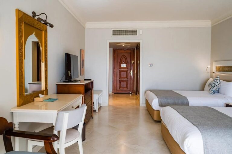 Una habitación con dos camas, un escritorio blanco y un espejo dorado en forma de arco