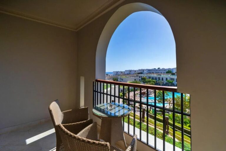 Un balcón bajo un arco, con dos sillones trenzados, sobre las piscinas y los jardines