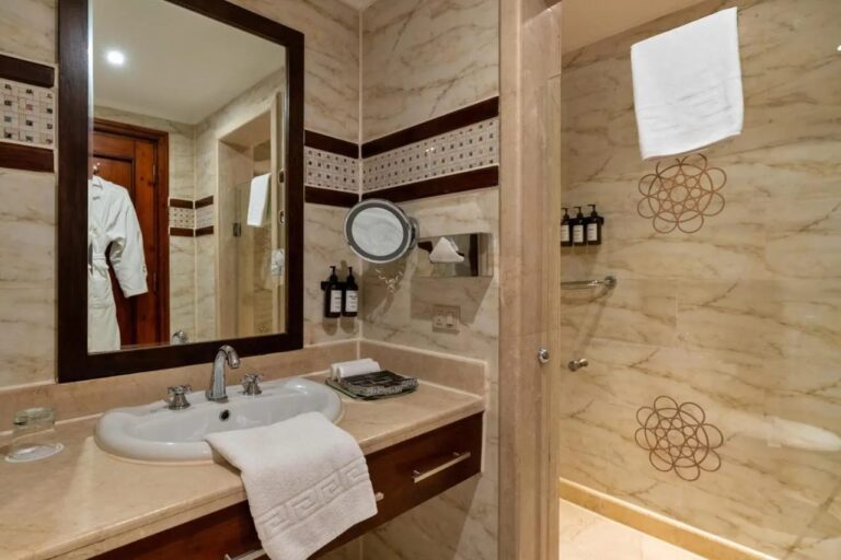 Un baño claro con lavabo, espejo de marco oscuro y ducha de cristal