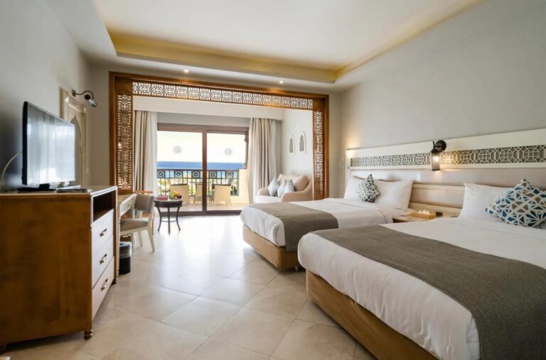 Una habitación con dos camas grandes, una zona de estar bajo un arco de madera y un balcón frente al mar