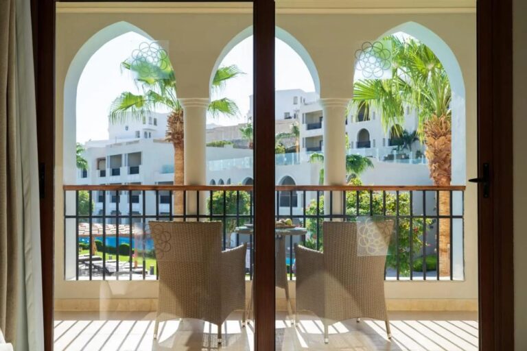 Un balcón con arcadas y dos sillones trenzados, frente a las palmeras y los edificios blancos del Sunrise Arabian Beach Resort
