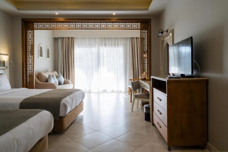 Una habitación con dos camas, una cómoda, una televisión y una zona de estar ante el ventanal