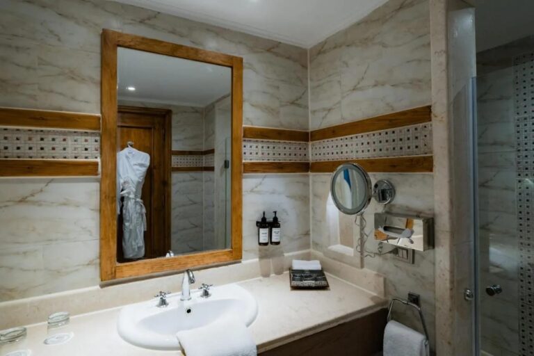 Un baño con lavabo, espejo con marco de madera clara y friso de mosaico