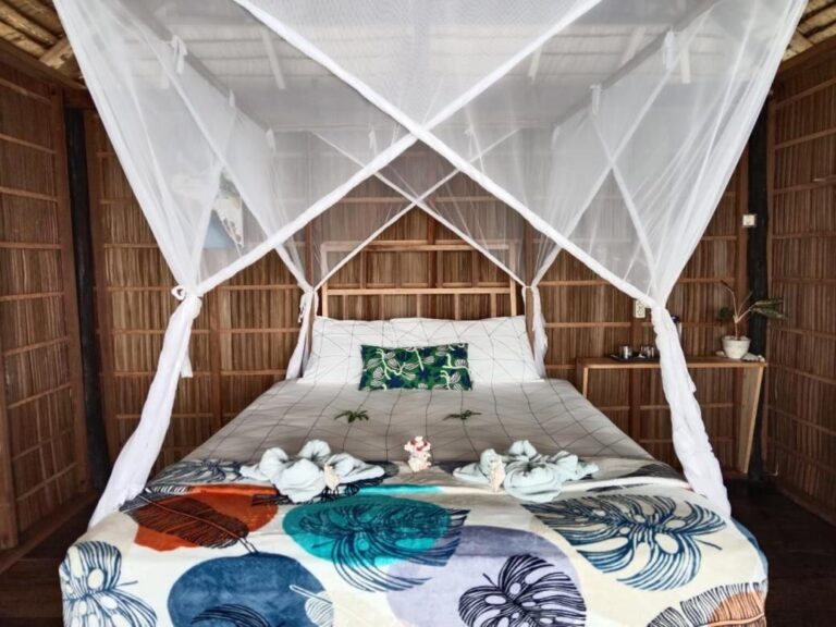 Una cama con mosquitero, una colcha de hojas azules y toallas dobladas