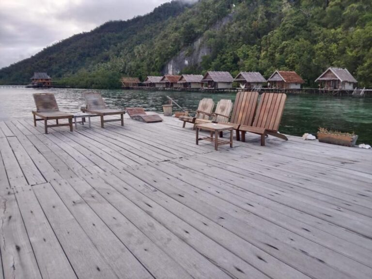 Sillones de madera y una mesa baja sobre un pontón, frente al acantilado y al bosque