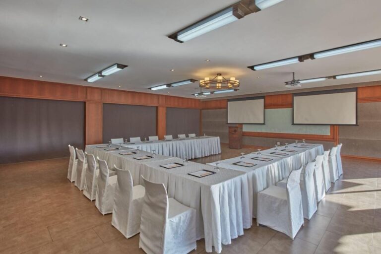 Una sala de reuniones con mesas en U con manteles blancos y dos pantallas de proyección