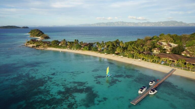 Vista aérea de la playa, del embarcadero con tres barcos y de un pequeño catamarán de vela