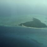 La isla Misali vista desde el avión, un triángulo de bosque bordeado por una playa blanca, sobre una plataforma arrecifal turquesa en medio de un mar azul oscuro, entre la bruma