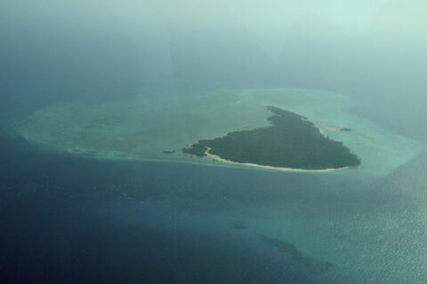 La isla Misali vista desde el avión, un triángulo de bosque bordeado por una playa blanca, sobre una plataforma arrecifal turquesa en medio de un mar azul oscuro, entre la bruma