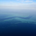 Vista aérea de un canal azul oscuro en forma de S que serpentea entre las plataformas turquesa de la barrera de coral, con algunos barcos blancos pequeños en el paso