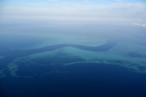 Vista aérea de un canal azul oscuro en forma de S que serpentea entre las plataformas turquesa de la barrera de coral, con algunos barcos blancos pequeños en el paso