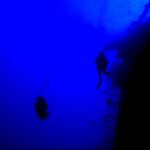 En un azul profundo, dos buceadores a contraluz recorren la barandilla de la popa del Salem Express, con la cubierta inclinada a la derecha