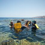 Nadadores con chalecos amarillos, máscaras y tubos en el agua clara del Blue Hole, con las montañas del Sinaí detrás